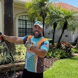 Eli of Sandbar Soft Wash, smiling in a branded jersey while rinsing a walkway on a Tampa Bay job