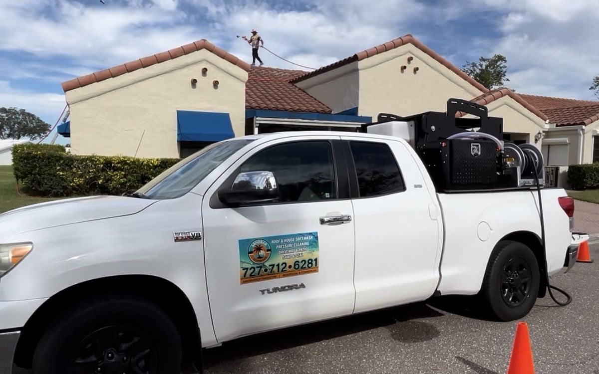 Sandbar Soft Wash truck and rig on site while a crew member soft washes the tile roof behind — real job photo